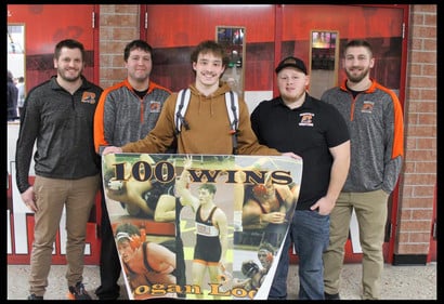 student holding 100 win banner with coaches